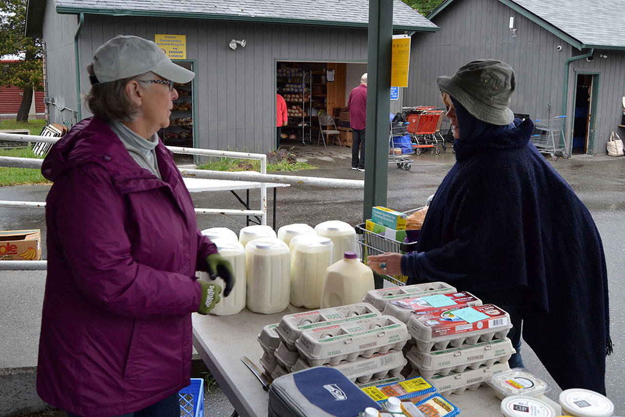 Bonnie Dickmann, a Sequim Food Bank dairy volunteer, helps Victoria Tamblyn receive a gallon of raw milk on May 20. Tamblyn said she has lived on a farm and believes raw milk has good health benefits. Dungeness Valley Creamerys raw milk was recently OKd by Clallam County health officials to be given out at the food bank so long as there were signs posted about the dangers of consuming raw milk. Sequim Gazette photo by Matthew Nash