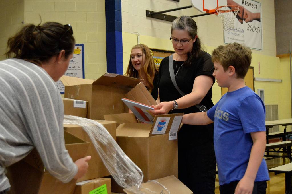Volunteers, from left, Kelsey Horst, Robyn Bacchus, Christina Crabb, and Louis Crabb pull and begin to sort books on May 22 in Helen Haller Elementarys cafeteria. By the end of the afternoon, thousands of books were bagged for each student to take home as part of the Six Books for Summer program.