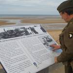 An unidentified World War II reenactor in uniform reading a commemorative sign overlooking the Normandy beach designated Omaha Beach by Allied strategists for the D-Day invasion. Photo submitted by Mac Macdonald.