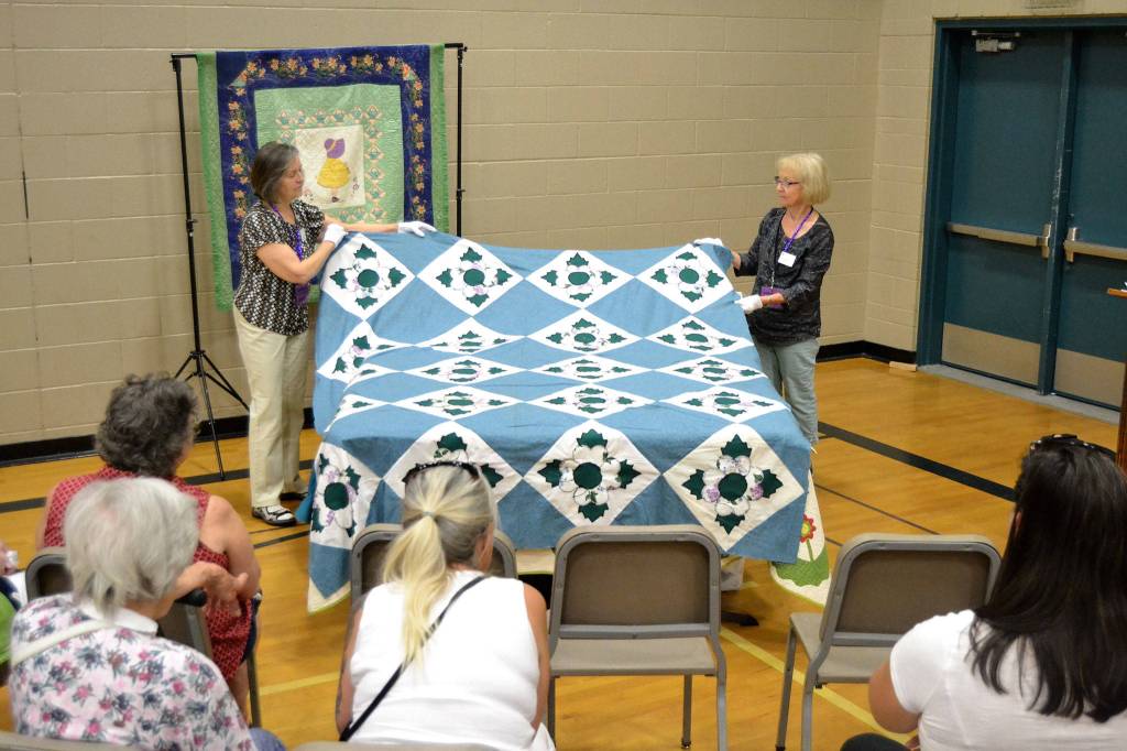 At last years quilt show, Barbara McArthur, left, and Nancy Davison of the Sunbonnet Sue Quilt Club turn a quilt made by Laura Hutzlers at-the-time 97-year-old grandmother. More antique quilts go on display this weekend. Sequim Gazette file photo by Matthew Nash