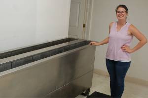 Brianne Moores of Moores Blind Cleaning stands with her companys ultrasonic blind cleaning machine. The eight-foot long machine can work with multiple sets of blinds at a time, and cleans them thoroughly using a combination of a mild cleaning solution and ultrasonic waves. Sequim Gazette photo by Conor Dowley