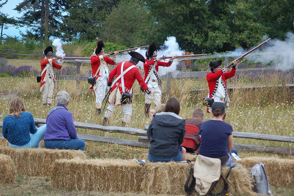 Left: The reenactors portraying the British Army fire on the Colonial Minutemen at the Battle of Concord Bridge while the crowd watches on during the Northwest Colonial Festivals portrayal.                                 Below: David Rieve, right, discusses Revolutionary War-era gunsmithing with several families in his tent at the Northwest Colonial Festival. Rieve, who is a trained gunsmith and has made numerous muskets and firearms that would be found in that era, has been coming to the Colonial Festival for several years and said that he enjoys the experience. Sequim Gazette photos by Conor Dowley