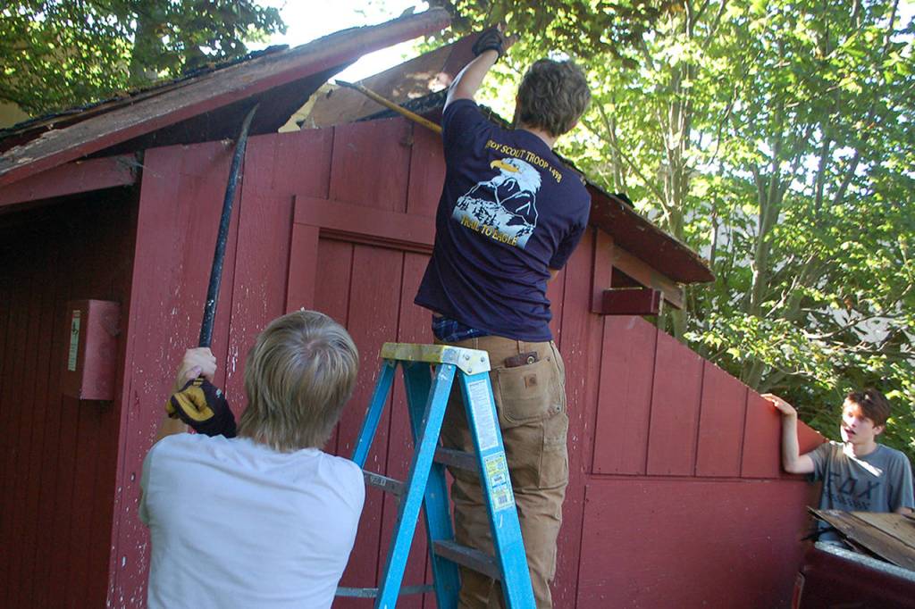 Eagle scout candidate Ian Thill, right, removes a section of the Pioneer Memorial Park storage sheds roof while Dylan Washburn, left, supports a larger section with a prybar. Washburn is an Eagle Scout himself and said that he wanted to lend his experience and support to his friend going through the same process. Sequim Gazette photo by Conor Dowley