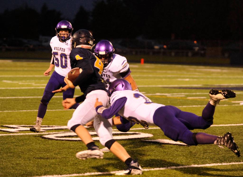 Forks quarterback Carter Windle (4) tries to evade the tackles of Sequims Truman Nestor (foreground) and Lane Mote as Sequims Isaiah Cowan (50) looks on. Sequim Gazette photo by Michael Dashiell