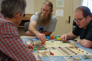 Travis Britten, second from left, demonstrates how to play the board game Robinson Crusoe to several Meeples of Sequim regulars who hadnt yet played it. Britten says that he regularly brings new games to teach as that kind of experience is a big part of gaming for him. Sequim Gazette photo by Conor Dowley