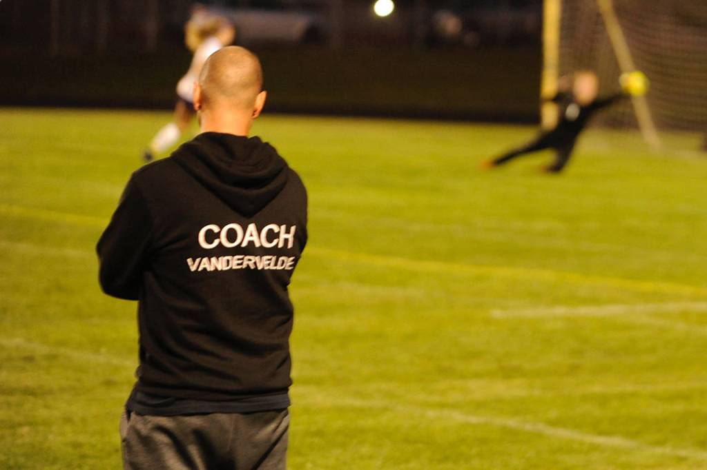 Sequim Wolves head coach Derek Vander Velde watches as goalkeeper Olivia Hale (background right) makes a diving save at the end of the first half of his teams match against North Kitsap. Vander Velde was upbeat after the match despite the loss, praising how well his players came together as a team to come from behind and force a penalty shootout. Sequim Gazette photo by Conor Dowley