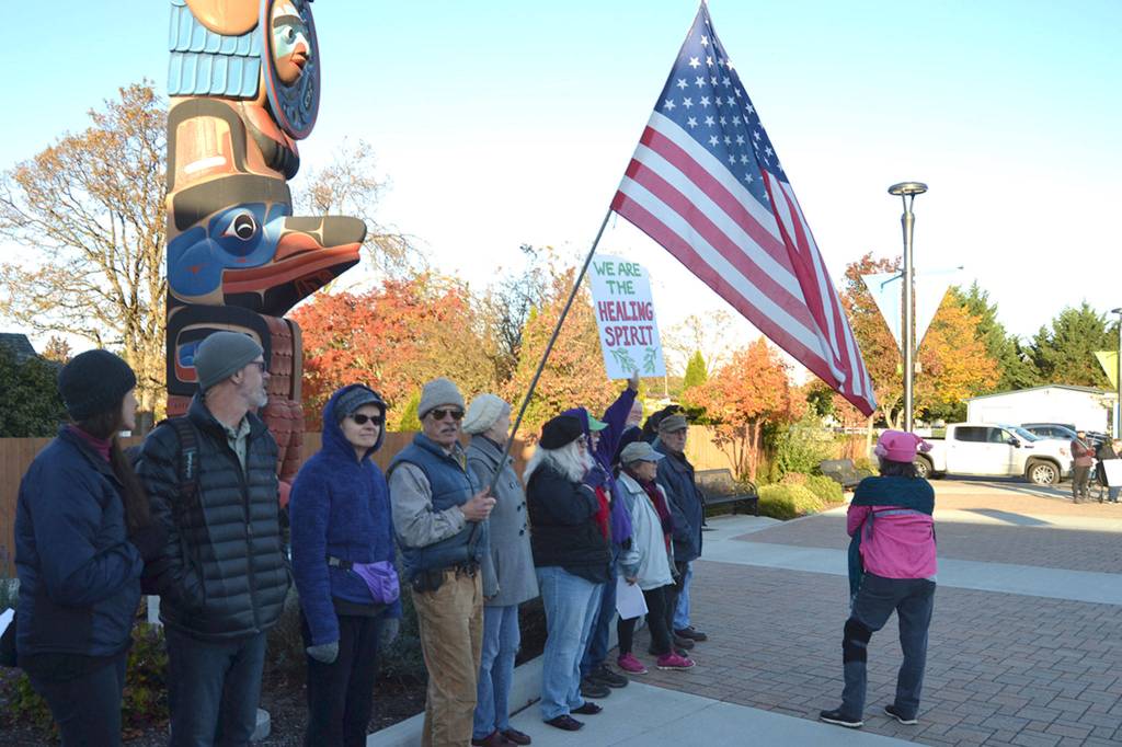 About a dozen people gather by the totem pole donated by the Jamestown SKlallam Tribe on Oct. 28 in support of the tribes proposed MAT clinic. The group, calling itself Voices for Health and Healing, sang hymns next to a large group of members of Save Our Sequim who oppose the MAT coming into Sequim. Sequim Gazette photo by Matthew Nash