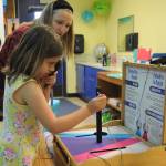 Helen Haller First-grader Eleanor Houseman tests her peripheral vision by threading a huge needle with one eye covered with assistance from parent helper Adrienne Christian.