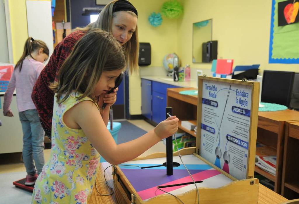 Helen Haller First-grader Eleanor Houseman tests her peripheral vision by threading a huge needle with one eye covered with assistance from parent helper Adrienne Christian.