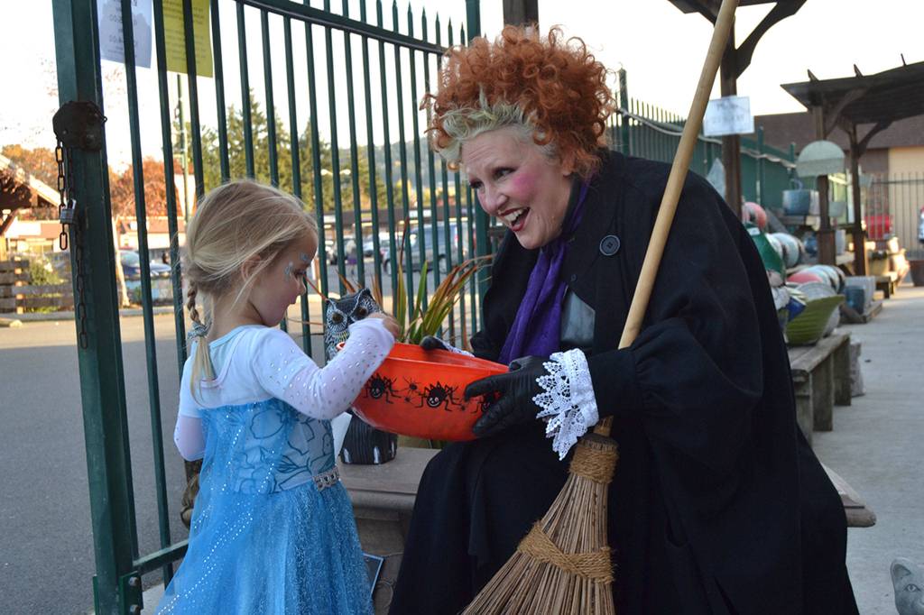 Below, Jody Nordby, an employee at The Co-Op Farm and Garden dresses as Winifred Sanderson from the Disney film Hocus Pocus to greet children on Halloween like Aubrie Huisman, 3, dressed as Elsa from Frozen.
