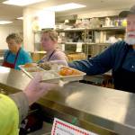 Doug Crabb of Sequim, right, hands out a dinner tray as volunteers, from left, Phyllis Meyer of Sequim, Linda Crabb of Sequim and Darci McCabe of Port Angeles prepare meals for Wednesdays Thanksgiving Eve lunch at the Port Angeles Salvation Army kitchen. (Keith Thorpe/Peninsula Daily News)
