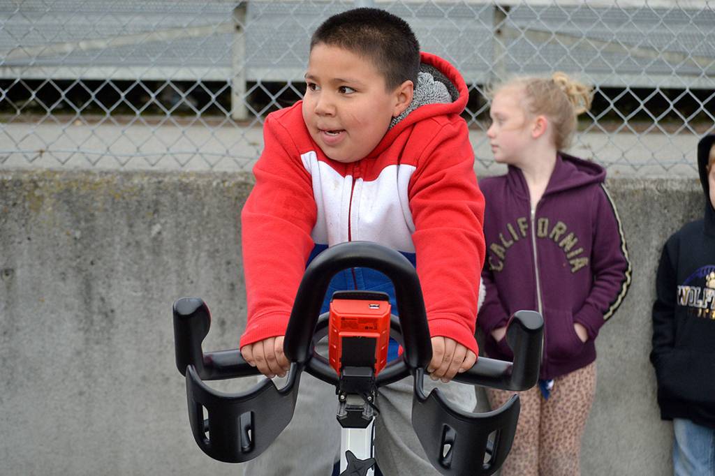 Second grader Damoni Gonzales rides an exercise bike care of the YMCA of Sequim to keep warm in-between laps during Helen Haller Elementarys Turkey Trot where cold winds made the event tough to traverse. Sequim Gazette photo by Matthew Nash