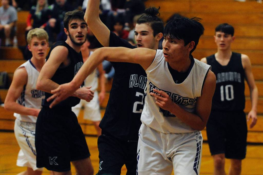 Freshman forward Isaiah Moore, second from right, passes the ball out from under the basket while under pressure from Klahowya Eagles forward Deven Patch during the Sequim Wolves 45-37 win over the Eagles on Dec. 2. Moore had eight points, eight rebounds and two blocks in his first high school game. Sequim Gazette photo by Conor Dowley