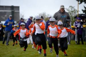 Players and coaches for the co-ed team of The Law Office of Alan Millet storm the field during the Player Procession at Sequim Little Leagues Opening Day in April 2019. Sequim Gazette file photo by Matthew Nash