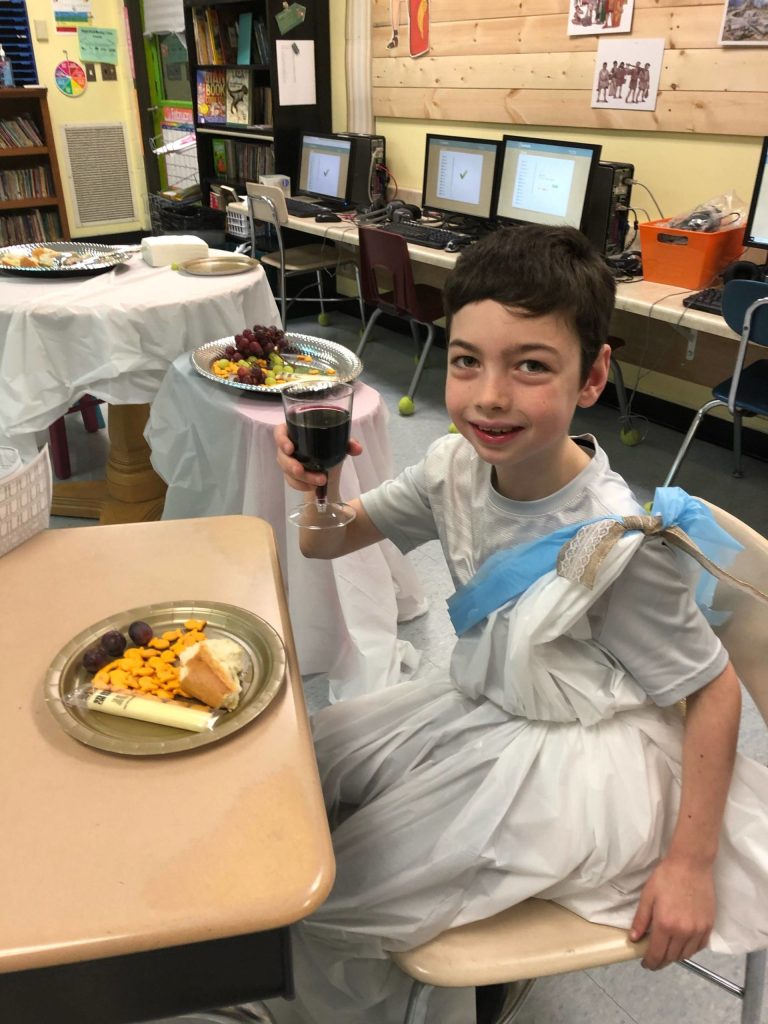 A toga-attired Blake Lawless raises a glass of fruit juice to symbolize a toast during ancient Roman times. A common Roman meal in ancient times included fish, cheese, bread and grapes. Photo by Robin Forrest
