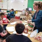 Teacher Heather Riley assists (from left) Seth Larson (back to camera), Trenton Hopson, Urijah Marchbanks and Clinton Cosio with assembling their mini pizzas, as James Bardin and Isaiah Johansen watch a video on how to make chocolate truffles. Photo by Melissa Sagara