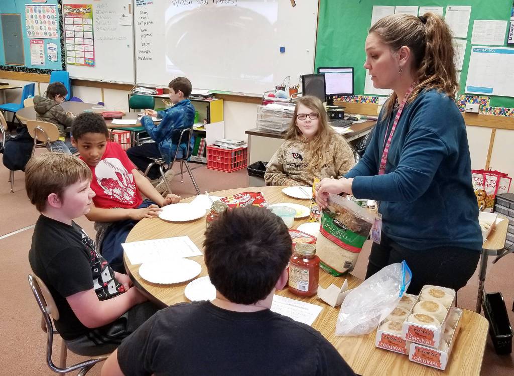 Teacher Heather Riley assists (from left) Seth Larson (back to camera), Trenton Hopson, Urijah Marchbanks and Clinton Cosio with assembling their mini pizzas, as James Bardin and Isaiah Johansen watch a video on how to make chocolate truffles. Photo by Melissa Sagara