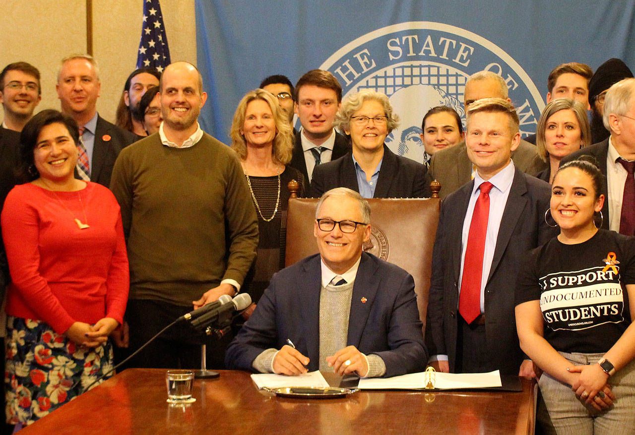 Gov. Jay Inslee, seated, signs the first bill of the 2020 legislative session into law. On the right stands the bills primary sponsor, Sen. Jamie Pedersen, D-Seattle, who is wearing a red tie. Photo by Cameron Sheppard/WNPA News Service