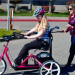 Alina Grieb, enjoys a ride on her new bike as physical therapist Cheri Bibler assists. Photo by Doug Schwartz