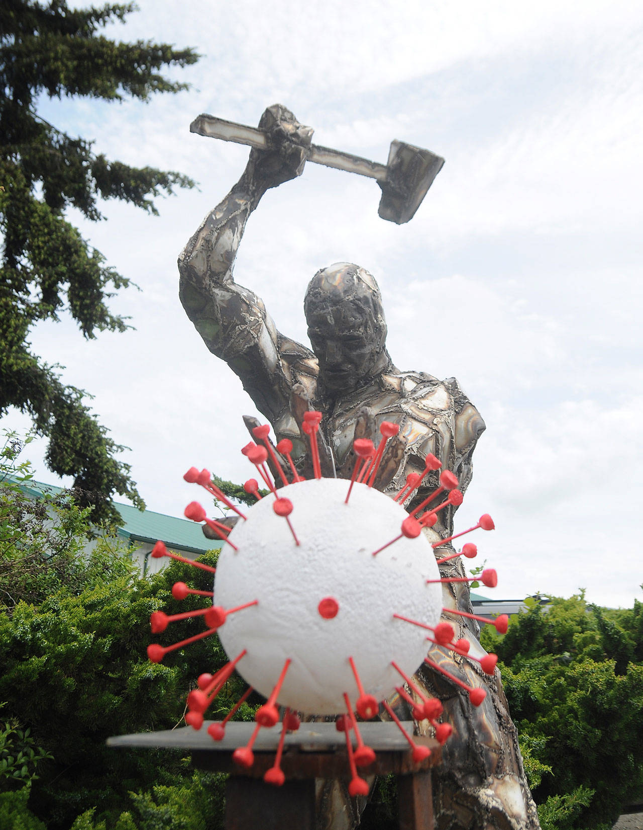 The 2019 novel coronavirus  an artists interpretation anyway  is under attack in Carlsborg. Bruce Cornett said he recently installed the virus-shaped art piece he and his wife Carol designed and created, as an addition to the original metal sculpture by comic book artist Per Berg. It was an idea that came to me some weeks back. We asked on the area Facebook forums for artists to take the idea and run with it … none did. So we did it ourselves. Dave Brasher, owner of High Energy Metals, commissioned Berg in 2012 to plan and piece together the intricate metal man for a display at the custom parts shop on Business Park Loop in Carlsborg. It seemed like a good fit for the ironwork, which is a remarkable piece, Cornett said. Sequim Gazette photo by Michael Dashiell