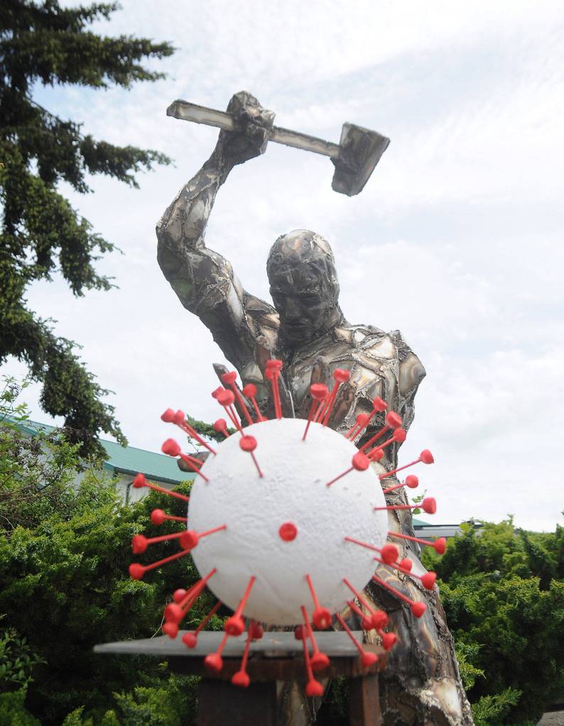 The 2019 novel coronavirus  an artists interpretation anyway  is under attack in Carlsborg. Bruce Cornett said he recently installed the virus-shaped art piece he and his wife Carol designed and created, as an addition to the original metal sculpture by comic book artist Per Berg. It was an idea that came to me some weeks back. We asked on the area Facebook forums for artists to take the idea and run with it … none did. So we did it ourselves. Dave Brasher, owner of High Energy Metals, commissioned Berg in 2012 to plan and piece together the intricate metal man for a display at the custom parts shop on Business Park Loop in Carlsborg. It seemed like a good fit for the ironwork, which is a remarkable piece, Cornett said. Sequim Gazette photo by Michael Dashiell