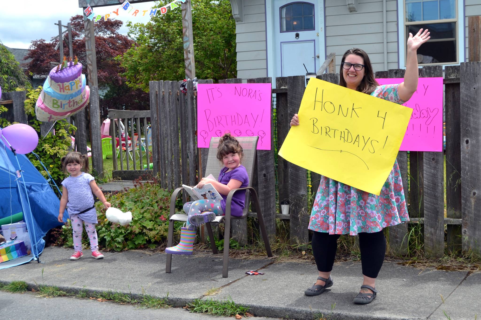 Mom Wynn Hannam holds a sign for drivers to honk for her daughter Noras third birthday on June 20. Nora, on left, waved to cars with her sister Ellie, mom, and dad Jared, not pictured.