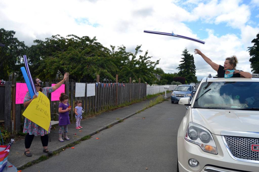 Grandma Keri Cook throws a pool noodle to daughter-in-law Wynn Hannam for granddaughter Noras birthday. The Hannam family, including Ellie, 5, and dad Jared, waved to drivers as theyd honk in celebration of the Sequim 3-year-olds birthday. Sequim Gazette photos by Matthew Nash