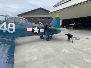 John Johnson, on left, with his wife Susie and crew chief Dave Richardson, and dog Kona, stand next to Johns T-6 Texan that he and Richardson will travel with on an aircraft to Hawaii and fly to commemorate the end of World War II 75 years ago. Photo courtesy of Kaye Gagnon