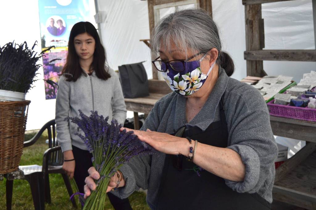 Above: Greg Hughes and Stephanie Lowe of Seattle take in some of the lavender scenery and beehives at Jardin du Soleil on July 19. It was their first time to the farm, and they heard about Sequim lavender farms remaining open on the radio. Sequim Below: June Devine, a retired Sequim teacher, works with Jaden Duan, 11, on lavender items to demonstrate what people can do with lavender at Washington Lavender on July 18. Devine usually makes and sell lavender products to help her granddaughter Emma pursue a dream of becoming an Olympic athlete. Duan was on the farm helping her grandparents, Dan and Janet Abbott, owners of Washington Lavender. Sequim Gazette photos by Matthew Nash