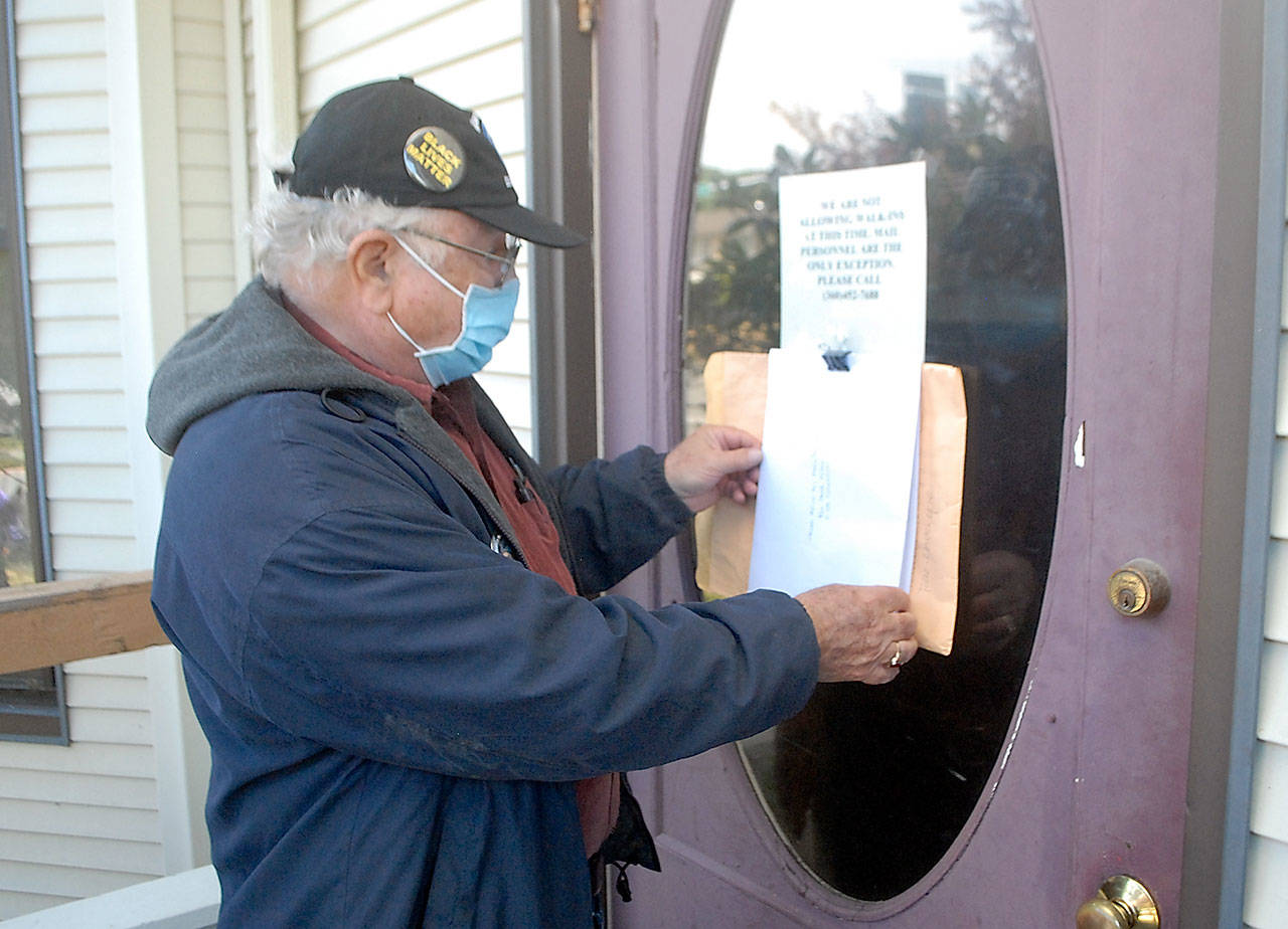 Tim Wheeler of Sequim, acting chairman of the non-partisan Voices for Health and Healing, attaches an envelope containing a letter on the front door of the building housing the Port Angeles office of U.S. Rep. Derek Kilmer on Thursday, July 23. The letter, signed by reportedly some 120 people, expressed disappointment in Kilmers progress in promoting universal health care, protection of Social Security and efforts to contain military spending, in particular the expansion of the U.S. Navys Growler aircraft training program at Naval Air Station Whidbey Island. Photo by Keith Thorpe/Olympic Peninsula News Group