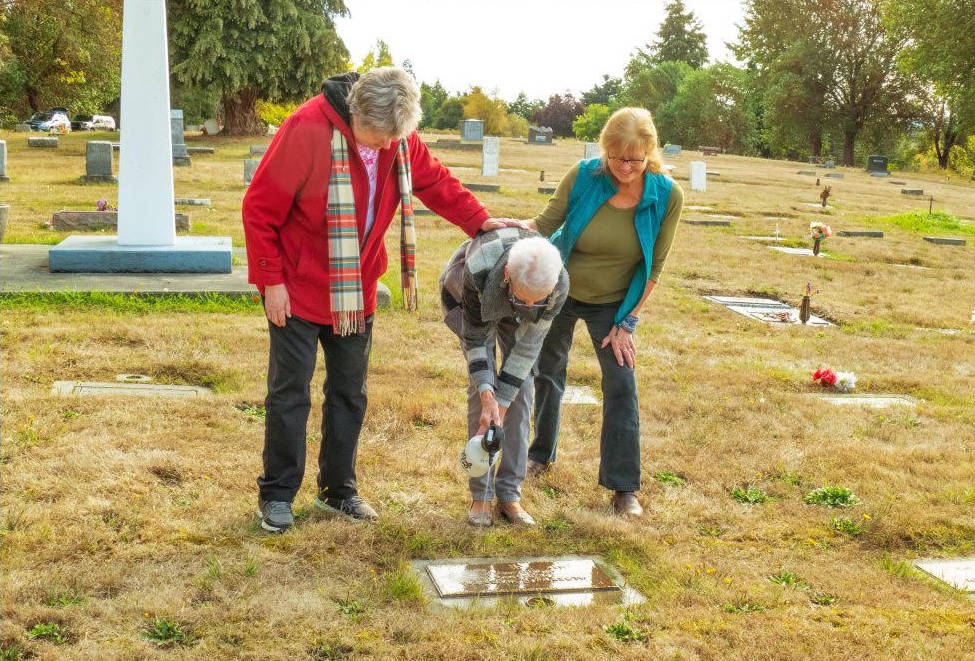 Family members Meri Ninetman, Linda Barnes Butcher and Tricia Bekkevar help clean the headstone of World War I veteran Albert O.Wagner (1892-1976) at Sequim View Cemetery.
