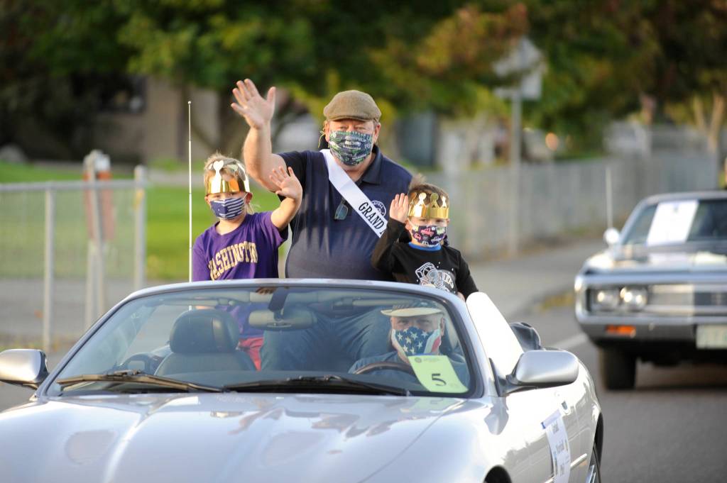 Grand Marshal Phil Castell, joined by grandsons Grayson Castell, left and Bennett Castell, waves to a virtual crowd and a few onlookers along Sequim-Dungeness Way during the Sequim Irrigation Festivals makeshift Grand Parade/Procession on Saturday, Oct. 10. John Coulson is pictured driving his classic Jaguar XK8. Sequim Gazette photo by Michael Dashiell