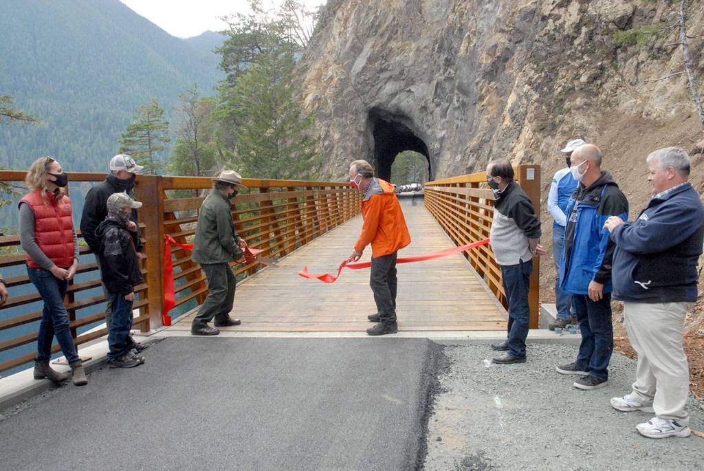 Lisa Turecek, facilities manager for Olympic National Park, and Rich James, former Clallam County Transportation Program Manager, wield ceremonial scissors to cut a ribbon to dedicate a reworked and refurbished Spruce Railroad Trail on the north shore of Lake Crescent on Thursday. (Keith Thorpe/Peninsula Daily News)
