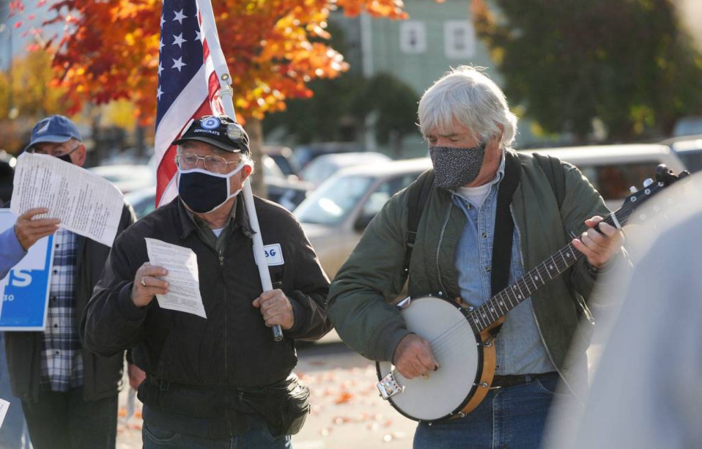 Tim Wheeler, left, and a group of about 40 individuals sing Woody Guthries This Land Is Your Land, accompanied by Steve Koehler on banjo, at the Sequim Civic Center on Nov. 4. The pair joined an event organized in part by Indivisible Sequim and part of a nation-wide rally to protect the results of the 2020 general election in case President Donald Trump refuses to concede. This is America; all our votes must count and be counted, said Elizabeth Schilling, event co-organizer. Sequim Gazette photo by Michael Dashiell