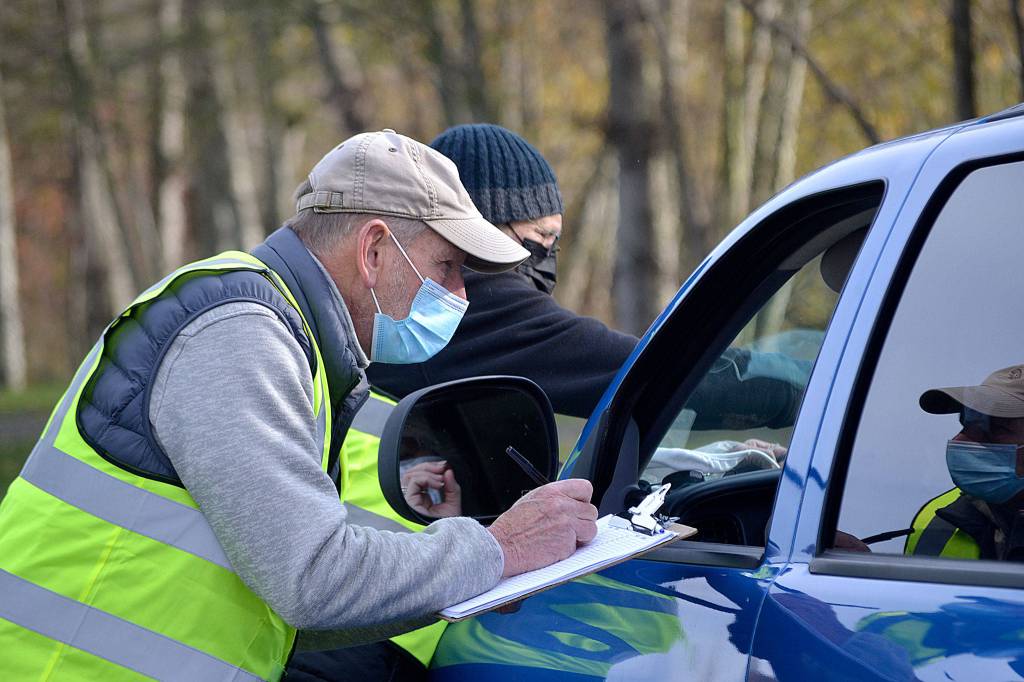 Volunteers Steve Allen and Bruce Winters check in a participant of the Family Holiday Meal distribution program on Nov. 20. Organizers estimate about 900 families received food packages. Below: Vehicles lined up from the Albert Haller Playfields to Washington Street to receive food. Sequim Gazette photos by Matthew Nash