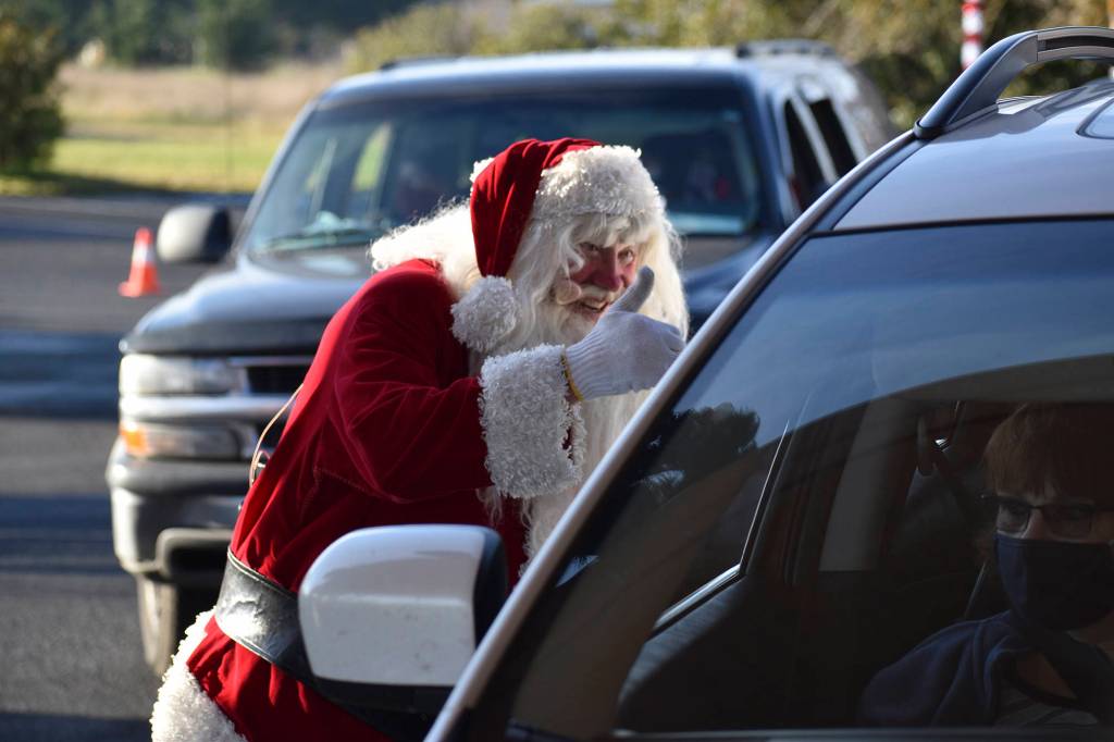 On the left, Santa Claus (Mac Macdonald) greets attendees of the Say Hello to Santa drive-by event Dec. 5 at Dungeness Valley Lutheran Church. Hosted by First Teacher and the Parenting Matters Foundation, the event saw youths receiving a goodie bag while spending a socially-distanced visit with
 Mr. Claus and his group of volunteer elves. Photo by Monica Berkseth