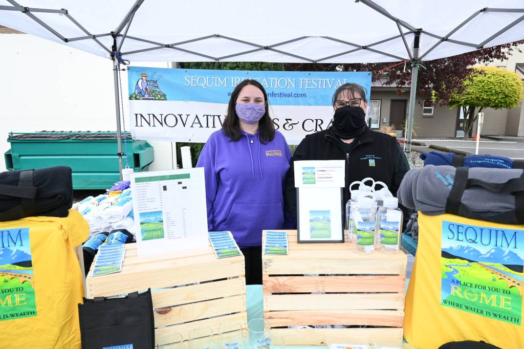 Kaitlyn Jackson, left, and Heidi Paulson help visitors to the Sequim Irrigation Festivals Innovative Arts and Crafts Fair in downtown Sequim get their festival swag. Sequim Gazette photo by Michael Dashiell