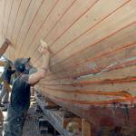 Last week, Shipwright Pete Steion of Port Townsend sands the bottom of the cutter Tally Ho in early May. Photo by Keith Thorpe/Olympic Peninsula News Group