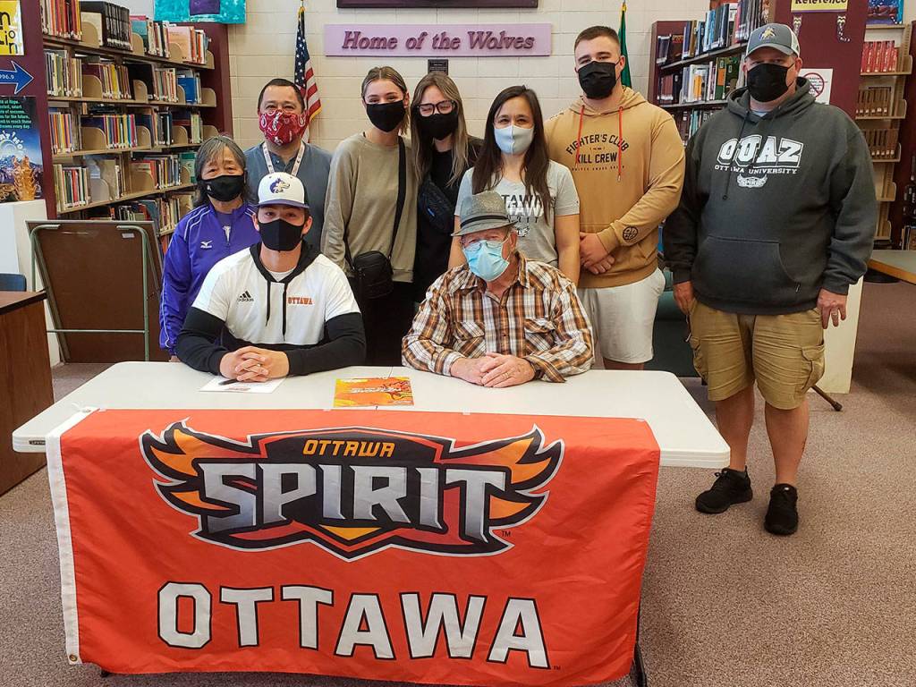 Michael Young, seated next to his grandfather Paul Arnbrister, announces last week his intent to play football at Ottawa University in Surprise, Ariz. Sequim High teammate Walker Ward also signed an intent to plat at Ottawa this fall. Pictured with Young are, back row from left, Kim Thompson, Denny Thompson, Kikayla Halady, Zoey Thompson, Diana Young, Johnnie Young and Chris Young. Submitted photo