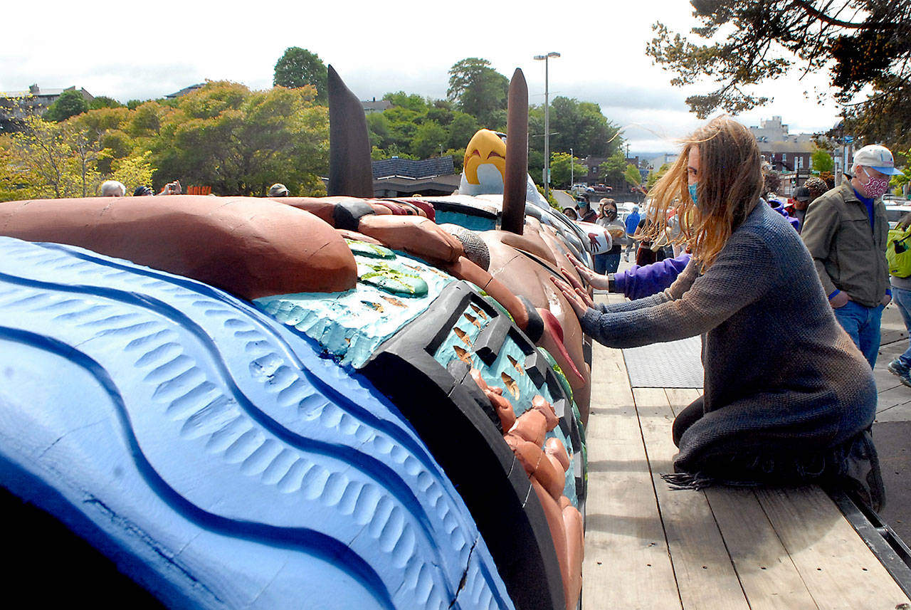 Julia Buggy of Sequim knees on a flatbed trailer as she lays her hands on a traveling totem created by carvers from the Lummi Nation during a stop on May 25 at Port Angeles City Pier. Photo by Keith Thorpe/Olympic Peninsula News Group