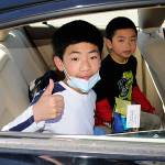 Can Bin Li gives a thumbs up with brother Can Hui Li behind him after participating in a drive-through graduation ceremony on June 17 for fifth-graders going to middle school.