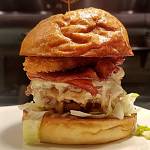 The Cowboy features three patties with Tillamook pepper jack cheese, applewood smoked bacon, house BBQ sauce, chopped onions, pickles, an onion ring, lettuce, and tomato on an artisan bun. Photo courtesy of Shadowline Burgers and Brews