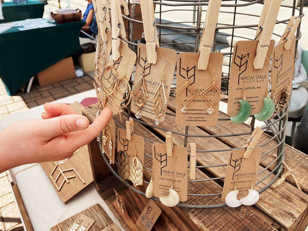 Above: Farmer-turned-artisan Erica Harris applies a natural chemical reaction to the surface of some of her raw brass pieces that highlights some brilliant tones of turquoise, greens and browns. Right: Harris brings her creative eye to offer wearable art at the Wheat Stalk Boutique booth, featured at the Sequim Farmers and Artisans Market this summer. Photos by Emma Jane EJ Garcia