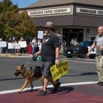 Two men, a dog, and a sign cross the intersection of Sequim Avenue and Washington Street during a loud protest on Aug. 18 against vaccine mandates for health workers. Sequim Gazette photo by Emily Matthiessen
