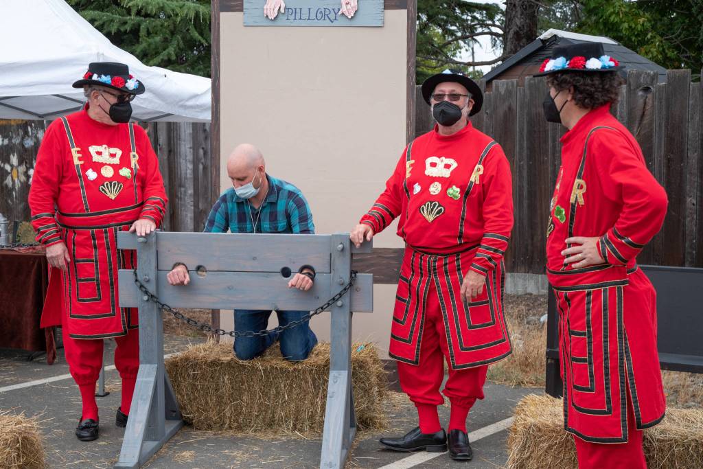 Beefeaters at the service of Queen Elizabeth I lock a man in the pillory after his companion paid a golden coin for the service at Olympia Theatre Arts Renaissance Faire on Aug. 22. Sequim Gazette photo by Emily Matthiessen