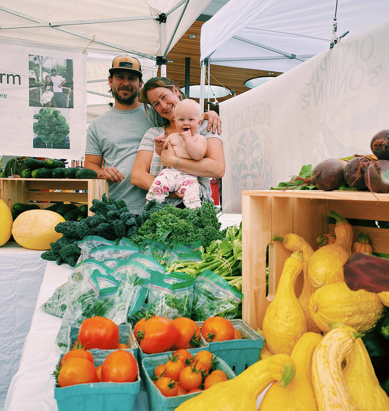 Rich Austin and Lindsey Soha, holding Rhea, offer a variety of edibles at the Rhea Sunshine Farm booth at the Sequim Farmers & Artisans Market. Photo by Emma Jane EJ Garcia