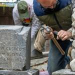 Using a chisel and hammer, Chris Smith chips away white mortar from the headstone of the infant son of R. and Eleanor Irwin, "God for him his angels sent," can be read. The inscription will become gradually more legible from being sprayed by volunteers with D/2 Biological Solution (TM). Next to the infant's headstone, sits that of George W. Caskedy. "Not a lot of information is available on Caskedy," said Priscilla Hudson, Sequim Prairie Garden Club historian, "because he was such a young kid. His father was W.M. Caskedy, born in Ohio. His mother Emma was born in Minnesota." Caskedy was fifteen when he died. Hudson said that there was no death certificate or newspaper reference, and nothing at the LDS family history center. "I'm assuming the father did logging," as they moved quite a bit, with residences in Blynn, Sequim, and Rema, all logging areas. George Caskedy's headstone was cleaned and reset in the corner of Pioneer Memorial Park with a collection of other headstones from the late 1800s to the early 1900s by volunteers this autumn. Sequim Gazette photo by Emily Matthiessen