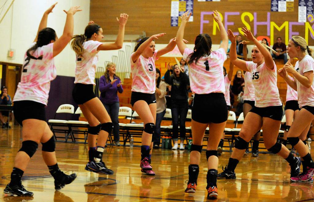 Sequim High volleyball teammates celebrate a key point in a 2015 match as head coach Jennie Webber Heilman (background, left) looks on.