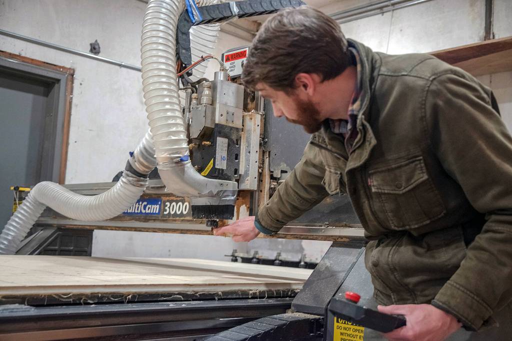 Martin Nerbovig of Camp N Car, a Port Townsend company started by Sequim High graduates in 2019, explains how the MultiCam 3000 machine has a series of bits for different work he programs it to perform, including a sharpie for marking the pieces customers will assemble in the kits Camp N Car sells across the nation for transforming the backs of vehicles into car campers. Sequim Gazette photo by Emily Matthiessen