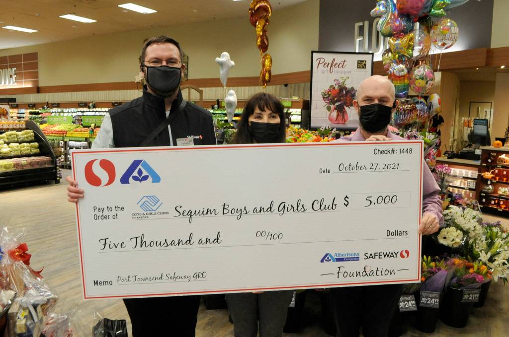 Joe Barton, Sequim Safeway store director, left, and Isaac Peiffer, assistant store director, present Mary Budke, executive director of the Boys & Girls Clubs of the Olympic Peninsula, a check to the Sequim branch $5,000 on Oct. 27 during a Grand Reopening celebration of the store. Sequim Gazette photo by Matthew Nash